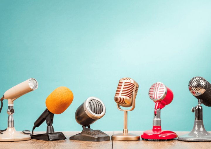 Photo illustrant une interview : 6 micros à pieds différents posés sur un bureau. Le fond est bleu ciel.