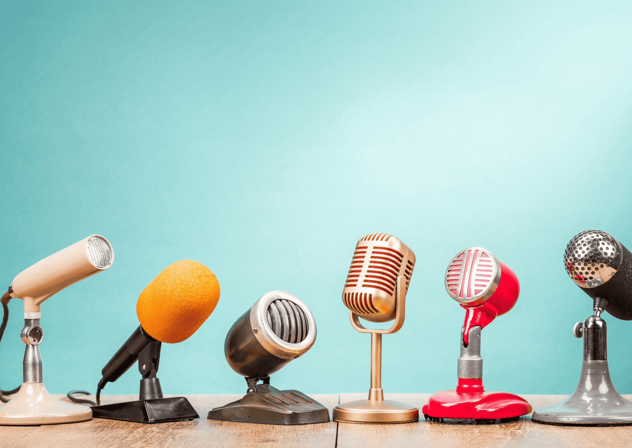 Photo illustrant une interview : 6 micros à pieds différents posés sur un bureau. Le fond est bleu ciel.